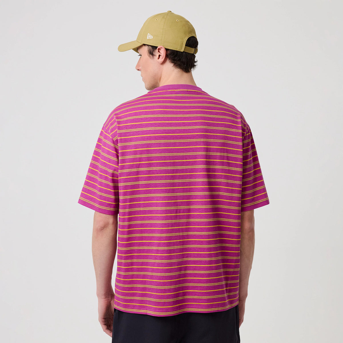 New Era Stripe Bright Purple T-Shirt, back view on a model wearing a light brown cap, featuring horizontal bright purple and yellow stripes across the entire back, with short sleeves and a relaxed fit.