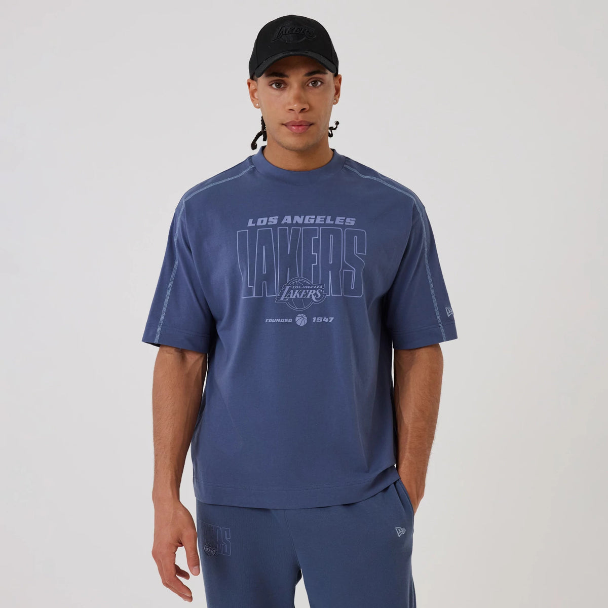New Era LA Lakers NBA Graphic Dark Blue Boxy T-Shirt, front view on-model showcasing a large printed Lakers logo across the chest, with 'Los Angeles' lettering above, complemented by a New Era logo embroidered on the left sleeve.
