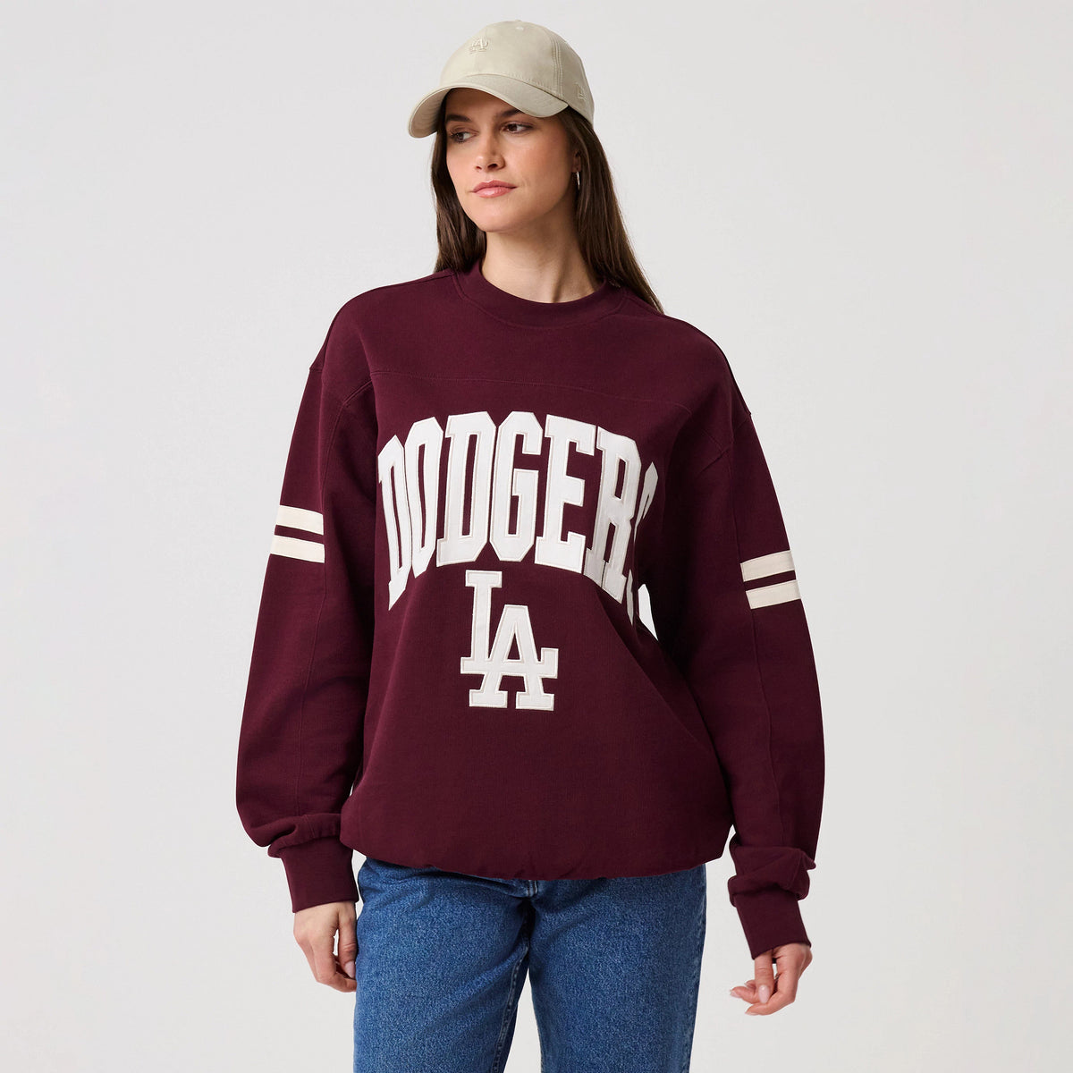 New Era LA Dodgers MLB Arch Graphic Dark Purple Crew Neck Sweater, front view on a model with a neutral baseball cap, showcasing white Dodgers lettering arching over LA on the chest and striped sleeve details for a sporty look.