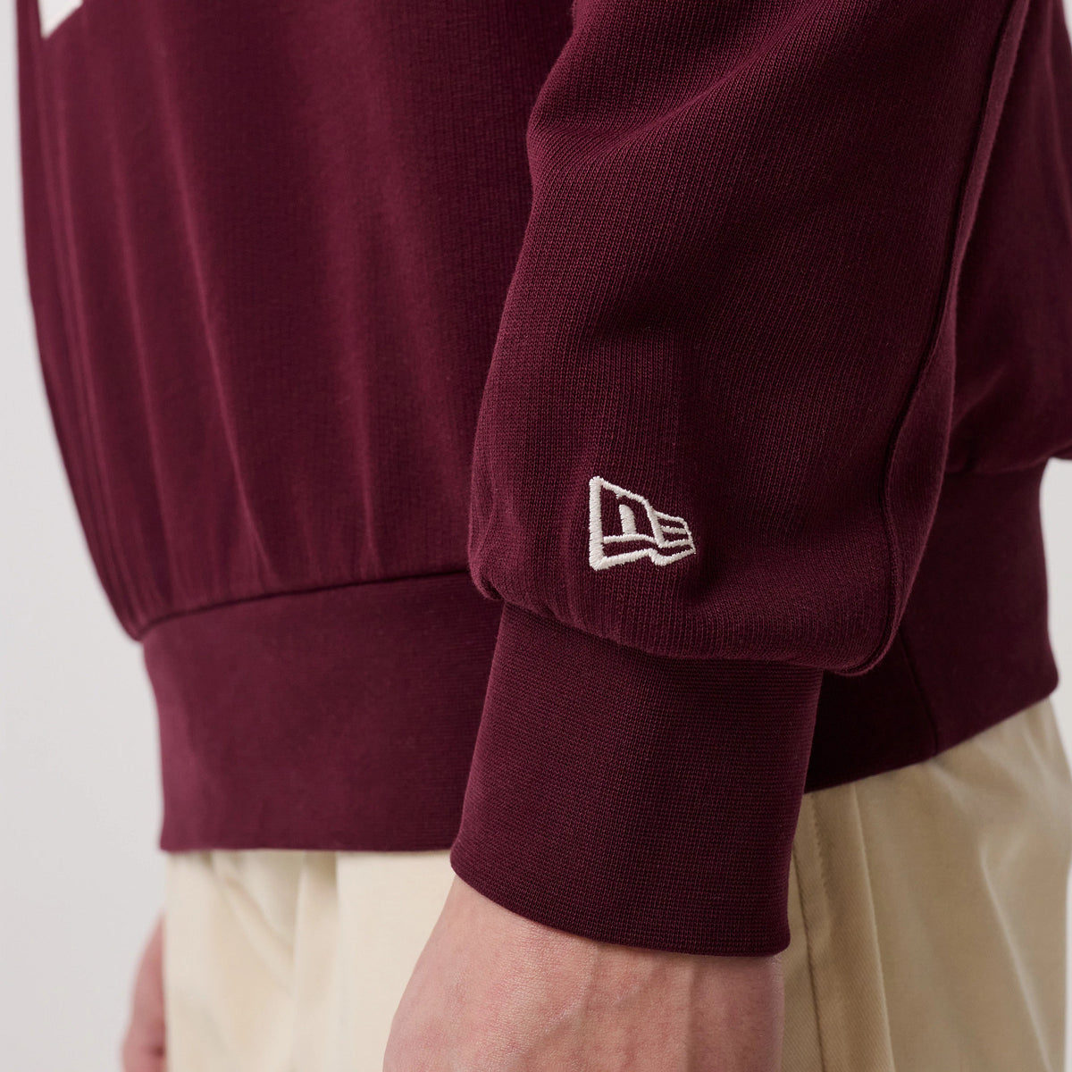 New Era LA Dodgers MLB Arch Graphic Dark Purple Crew Neck Sweater, side view showing the white embroidered New Era flag logo on the ribbed cuff of the dark purple sleeve, with a relaxed fit and soft texture.