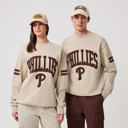 New Era Philadelphia Phillies MLB Arch Graphic Light Beige Crew Neck Sweater, front view on two models with matching light beige caps, showcasing large brown Phillies lettering and a P logo on the chest, complemented by double stripes on the sleeves.