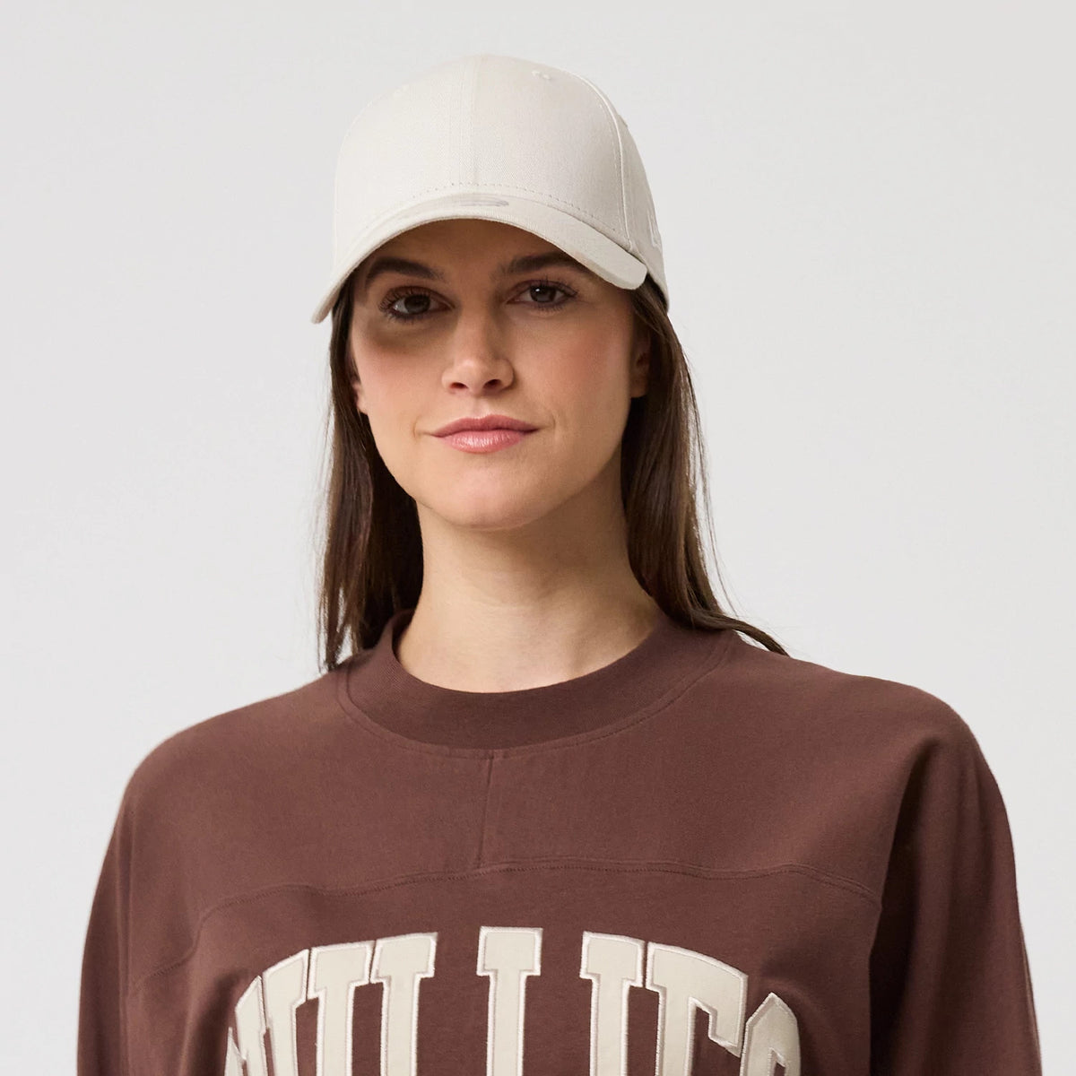 New Era Philadelphia Phillies MLB Arch Graphic Brown Oversized T-Shirt, front view on a model with a plain cream cap, featuring large embroidered Phillies lettering across the chest in cream set against the dark brown fabric.