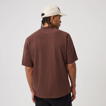 New Era Philadelphia Phillies MLB Arch Graphic Brown Oversized T-Shirt, back view on-model showcasing the plain brown back without graphics, loose fit and short sleeves, paired with a light-coloured cap contrasting the brown hue of the T-shirt.