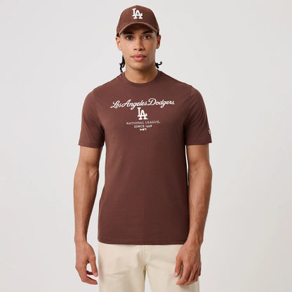 New Era LA Dodgers MLB Linear Brown T-Shirt, front view on a model with a matching brown cap, showcasing white embroidered Los Angeles Dodgers script across the chest, LA logo beneath, and New Era flag on the left sleeve.