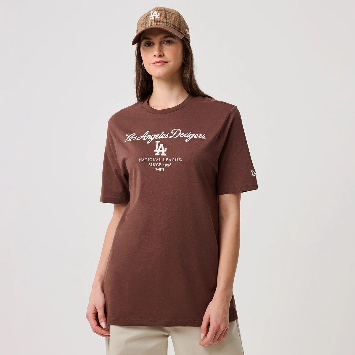New Era LA Dodgers MLB Linear Brown T-Shirt, front view on a model, featuring the white embroidered Los Angeles Dodgers script logo across the chest and a small embroidered New Era logo on the left sleeve, styled with a matching cap.
