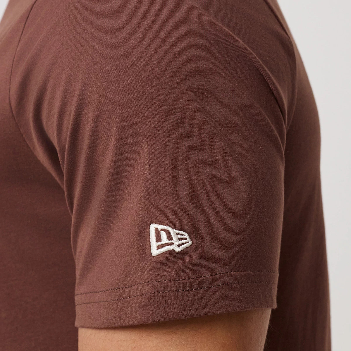 New Era LA Dodgers MLB Linear Brown T-Shirt, side view showing the close-up of the sleeve with an embroidered New Era logo in white near the cuff, highlighting the plain brown fabric and a seam along the arm.