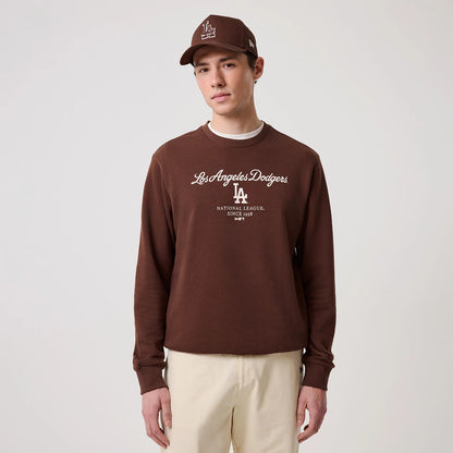 New Era LA Dodgers MLB Linear Brown Crew Neck Sweater, front view on a model wearing a matching brown cap, featuring white Los Angeles Dodgers script across the chest, the LA logo beneath, and ribbed cuffs and hem for a classic fit.