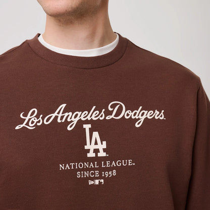New Era LA Dodgers MLB Linear Brown Crew Neck Sweater, front view on a model featuring white Los Angeles Dodgers script embroidered across the chest, complemented by the LA logo beneath and MLB branding near the hem, with ribbed crew neck collar.