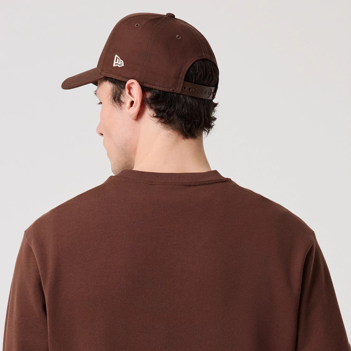 New Era LA Dodgers MLB Linear Brown Crew Neck Sweater, rear view on a model wearing a brown New Era cap, showing a plain brown back with ribbed collar and matching cap featuring a white New Era flag logo on the left side.