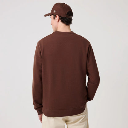 New Era LA Dodgers MLB Linear Brown Crew Neck Sweater, back view on a model wearing a matching brown cap, highlighting the solid brown fabric with ribbed cuffs and hem, creating a casual yet sporty look complemented by beige trousers.