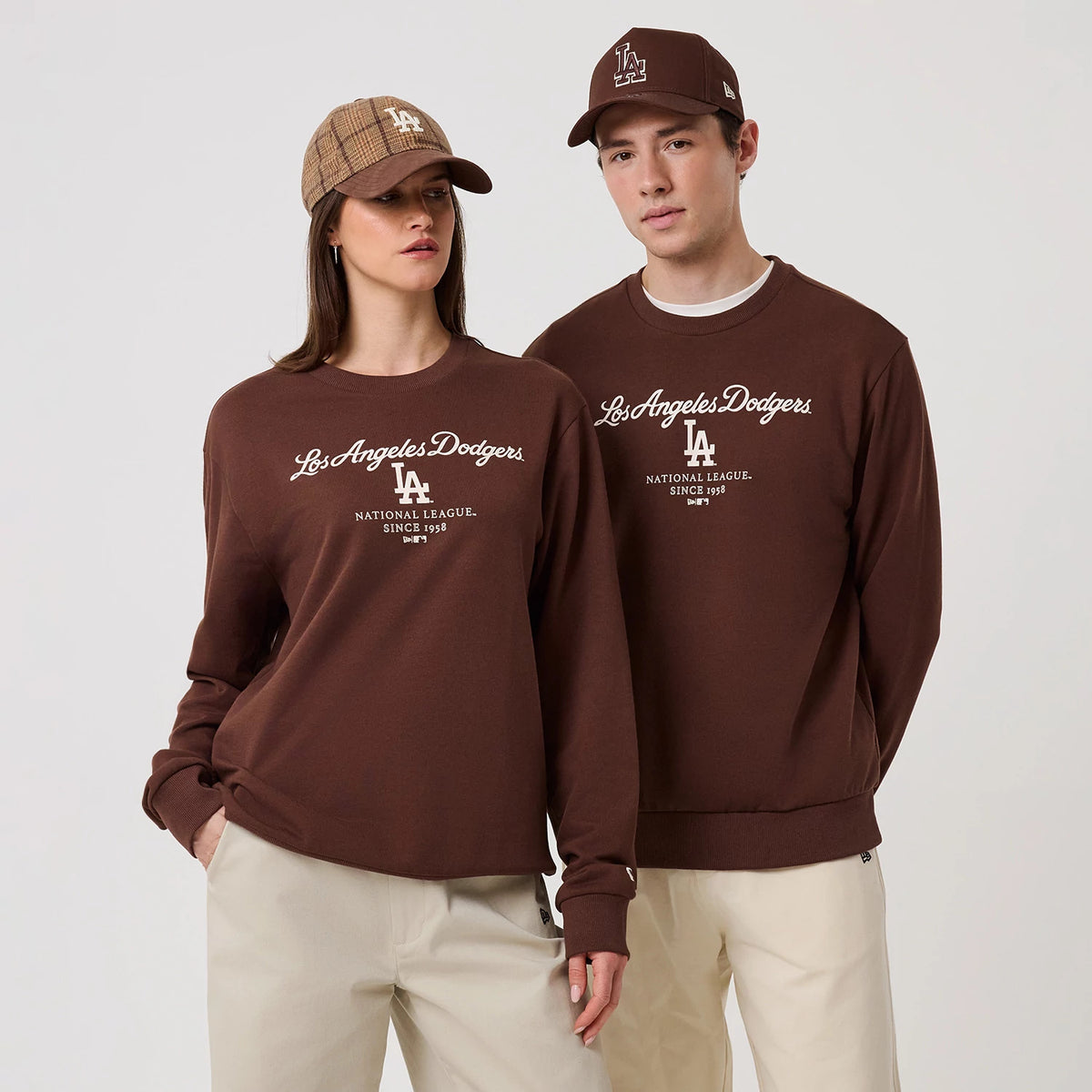 New Era LA Dodgers MLB Linear Brown Crew Neck Sweater, front view on a model with a matching brown cap, featuring the white embroidered Los Angeles Dodgers script and LA logo on the chest, with ribbed cuffs and hem.