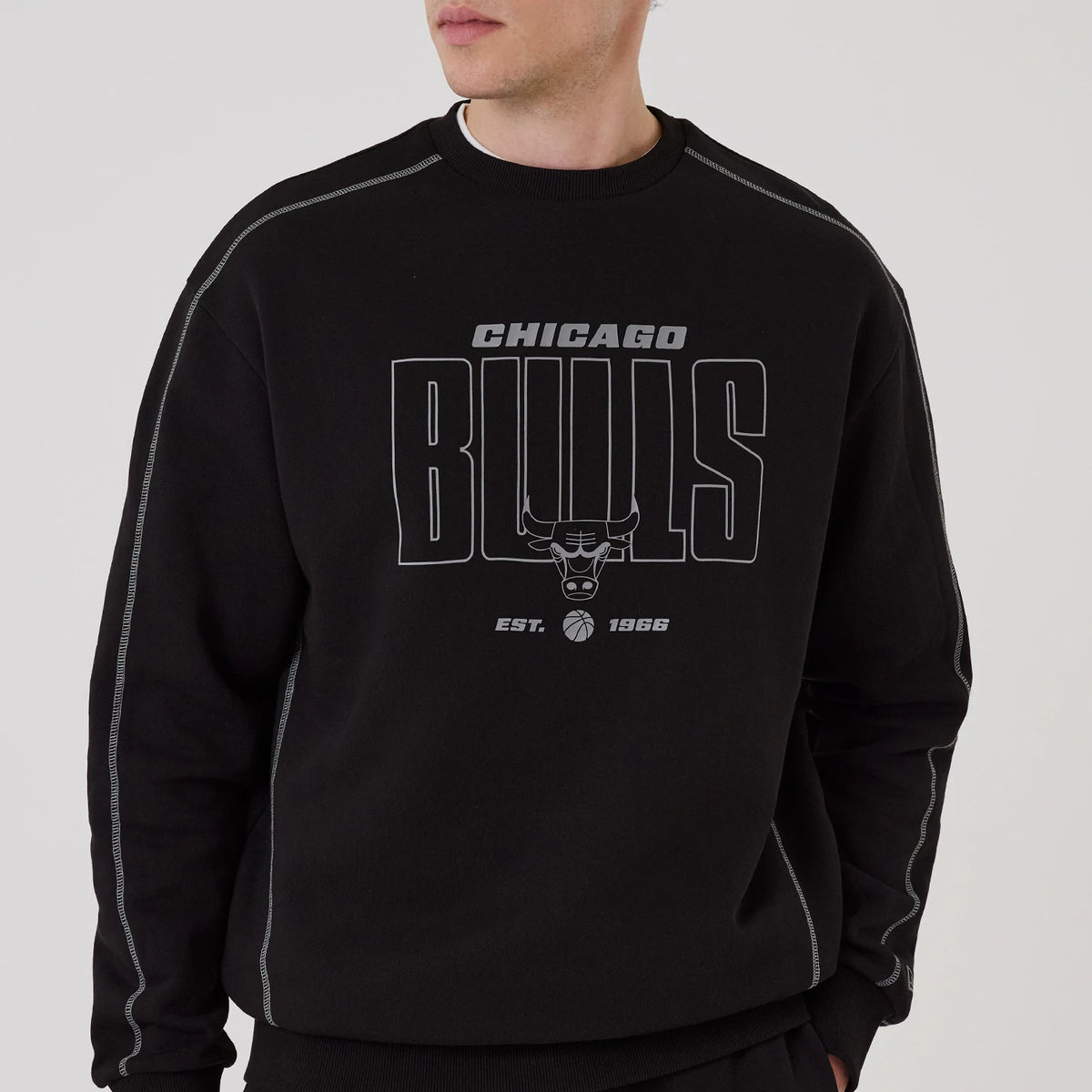 New Era Chicago Bulls NBA Graphic Black Crew Neck Sweater, front view on a model featuring a Chicago Bulls logo and lettering in grey print across the chest, with Est. 1966 and basketball graphic beneath, detailed stitching along the sleeves.