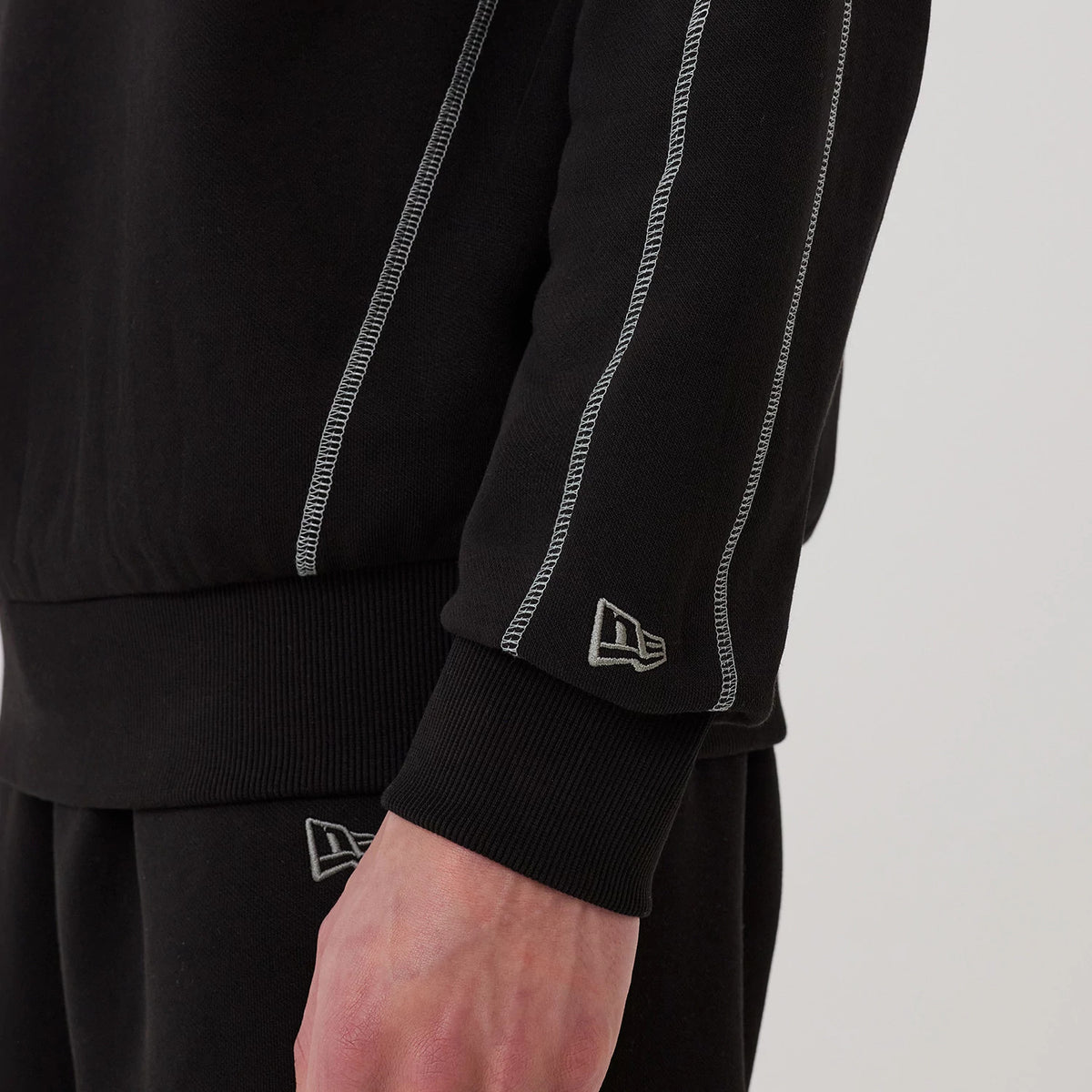 New Era Chicago Bulls NBA Graphic Black Crew Neck Sweater, close-up view on a model showing white contrast stitching along the arm seam, ribbed cuff detail, and the New Era flag logo embroidered in white near the wrist.