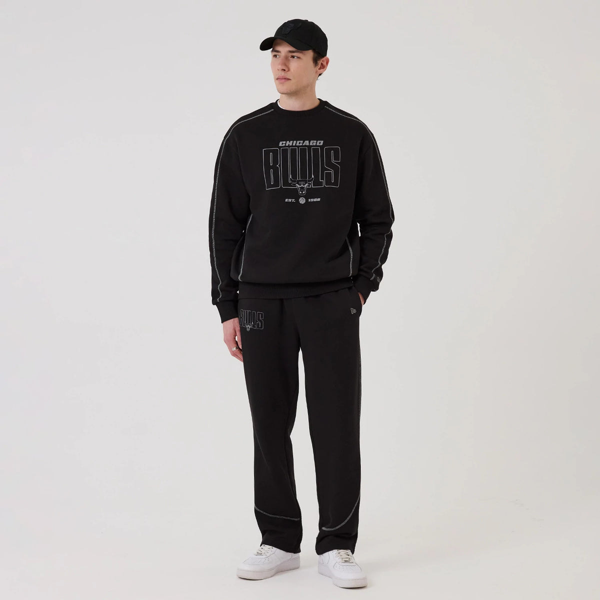 New Era Chicago Bulls NBA Graphic Black Crew Neck Sweater, front view on a model with a matching black New Era cap, featuring a large grey Chicago Bulls logo and script on the chest, and light grey on the sleeves.