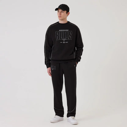 New Era Chicago Bulls NBA Graphic Black Crew Neck Sweater, front view on a model with a matching black New Era cap, featuring a large grey Chicago Bulls logo and script on the chest, and light grey on the sleeves.