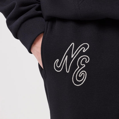 New Era Navy Straight Leg Joggers, close-up showing the embroidered script NE logo in white on the upper thigh, with a hand placed in the side pocket, and a ribbed cuff seen above the logo, highlighting the garment's textured material.