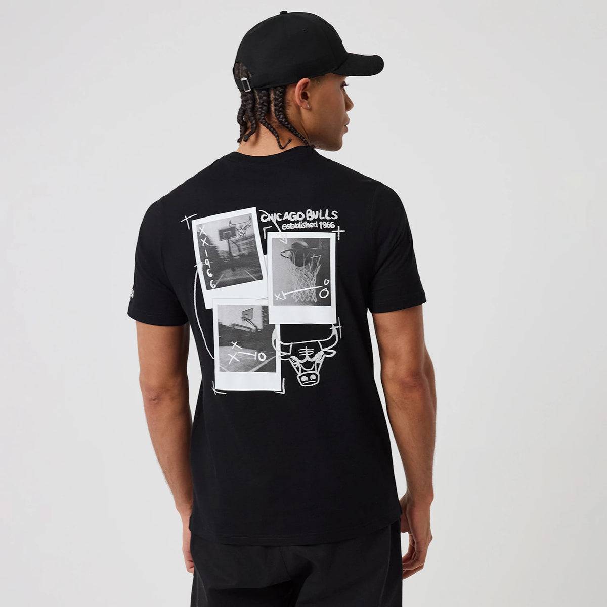New Era Chicago Bulls NBA Graphic Black T-Shirt, back view on a model with a black cap, featuring a large white graphic design including Chicago Bulls lettering, established 1966 text, and several basketball-themed images across the upper back.