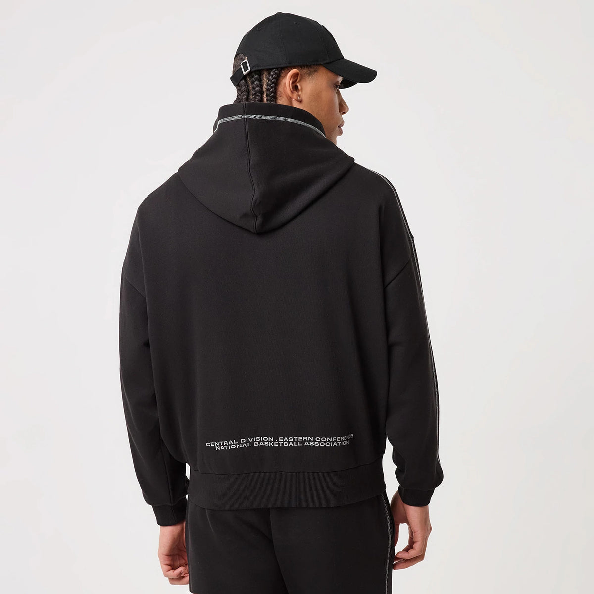 New Era Chicago Bulls NBA Graphic Black Pullover Hoodie, back view on-model showing the black hoodie with a spacious hood, prominent white printed text along the lower hem, and stitching details near the shoulders.
