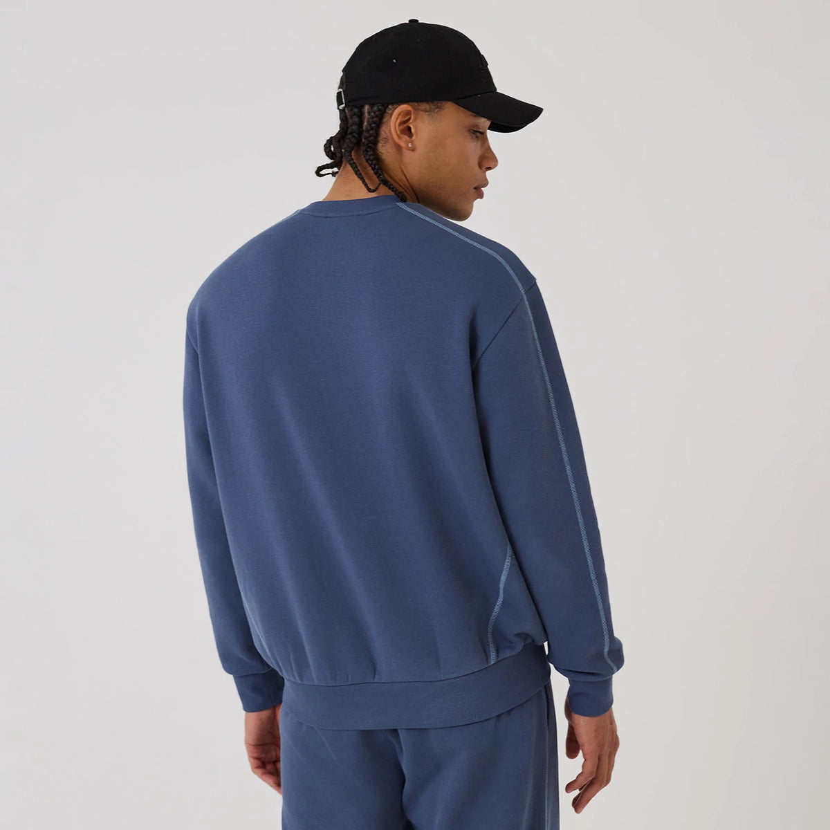 New Era LA Lakers NBA Graphic Dark Blue Crew Neck Sweater, rear view on a model wearing a black cap, showing the relaxed fit with ribbed cuffs and hem, and seam running down the sleeves for a appearance.
