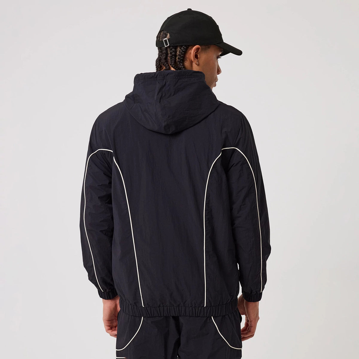 New Era New York Yankees MLB Piping Navy Track Jacket, back view on a model wearing matching navy trousers and a black cap, featuring a hood and distinctive white piping running along the shoulders and sides, with elasticated cuffs at the wrists.