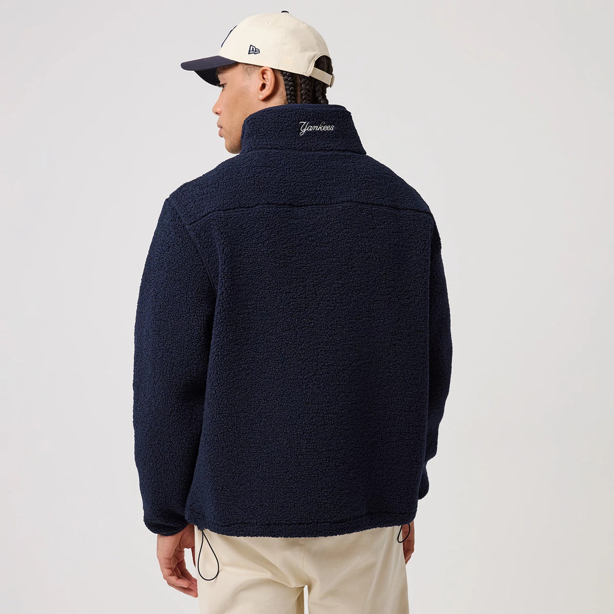 New Era New York Yankees MLB Dark Blue Sherpa Jacket, back view on-model highlighting the embroidered Yankees lettering on the upper back of the dark blue textured jacket, worn with light trousers.