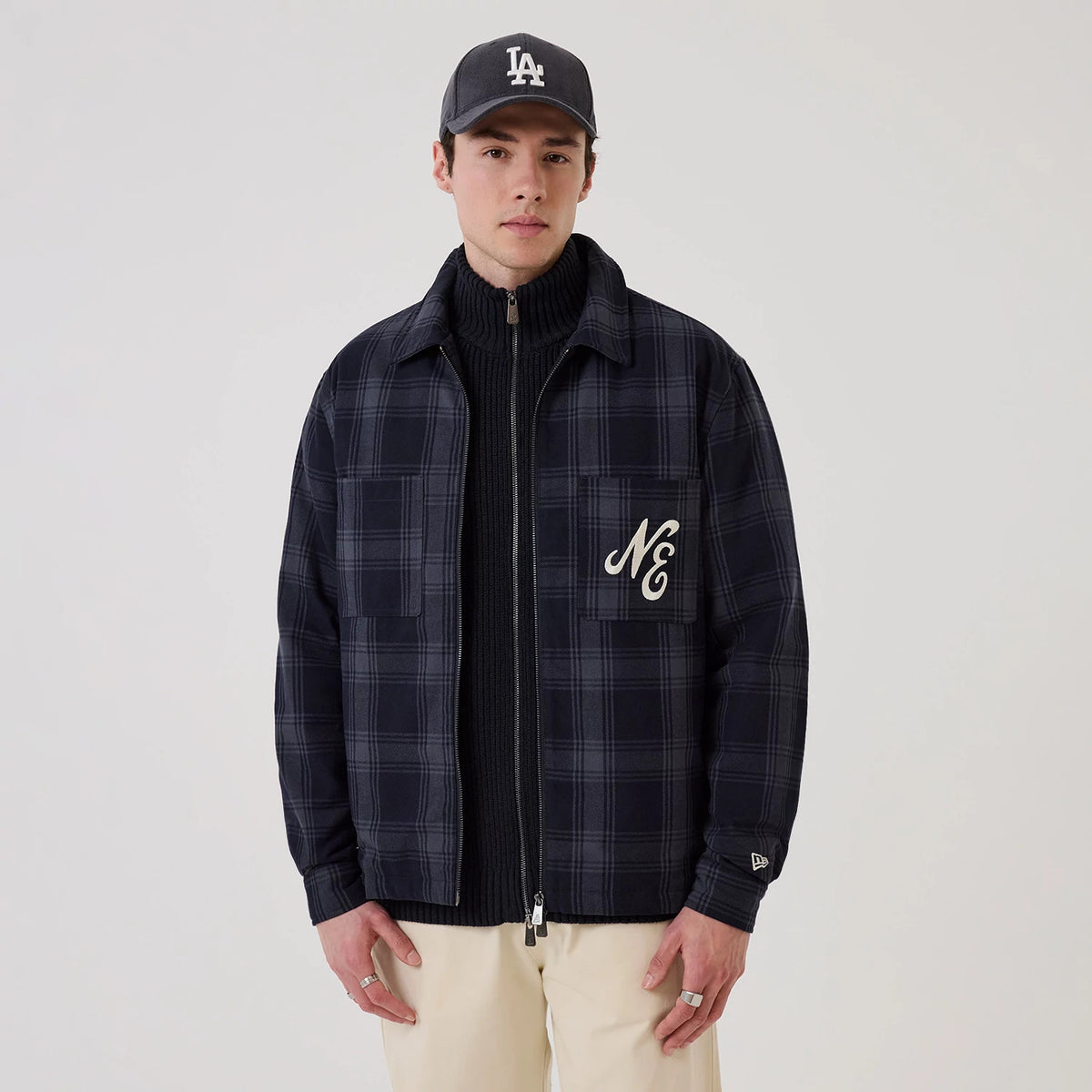 New Era Navy Shacket, front view on a model wearing a dark cap, featuring a navy plaid pattern, an embroidered NE logo on the left chest pocket, and a New Era flag logo on the left sleeve cuff.