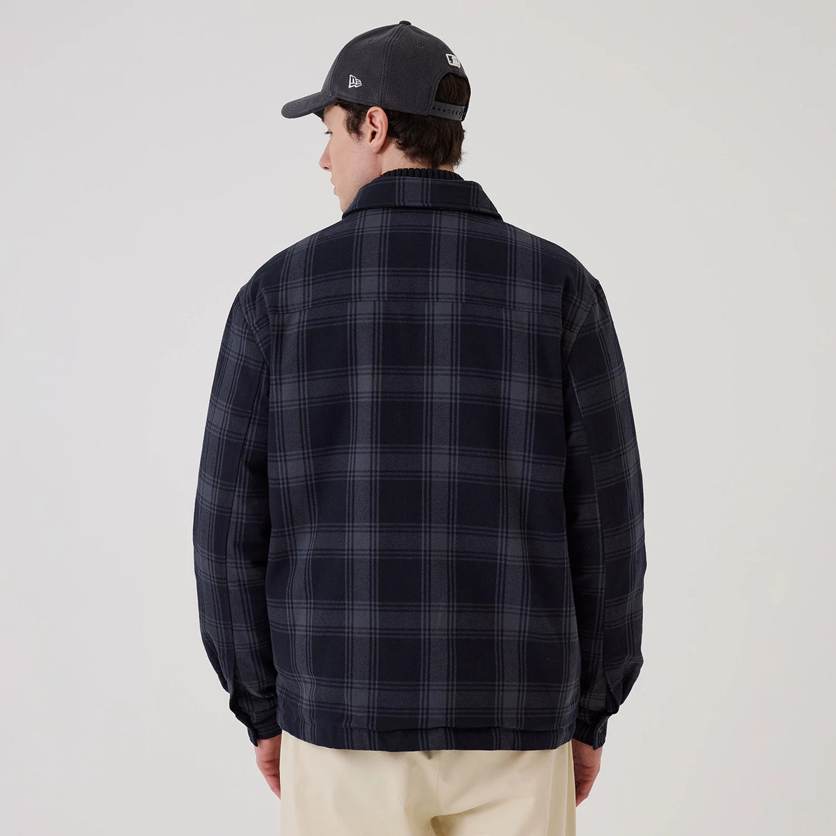 New Era Navy Shacket, back view on a model wearing a grey cap, showcasing the dark navy and grey plaid pattern across the entire surface of the shacket, structured collar, and relaxed fit over beige trousers.