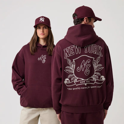 New Era Crest Graphic Dark Purple Pullover Hoodie, front and back view showing the embroidered NE crest logo on the front left chest and a large graphic on the back with New York lettering above a crest, worn with a matching dark purple cap.