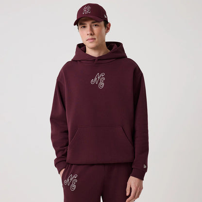 New Era Crest Graphic Dark Purple Pullover Hoodie, front view on-model showing an embroidered NE logo on the chest, a large kangaroo pocket at the front, and a small embroidered New Era logo on the left sleeve cuff.