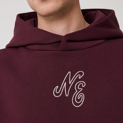 New Era Crest Graphic Dark Purple Pullover Hoodie, front view showing a large hood and a prominently embroidered NE logo in white on the chest, with the dark purple fabric creating a contrast.