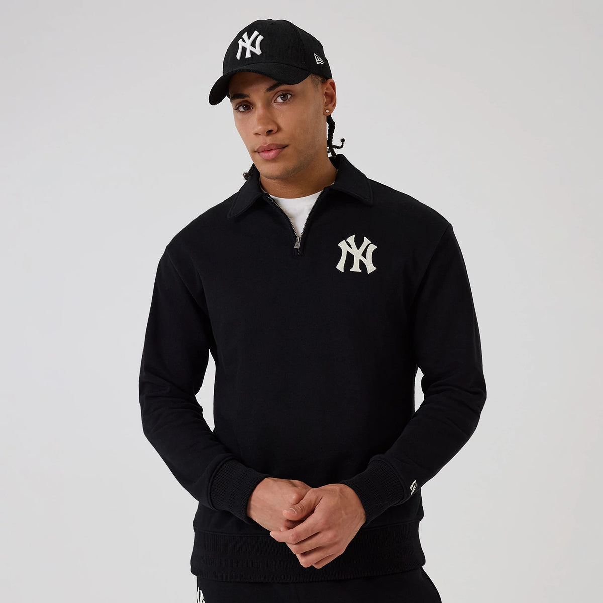 New Era New York Yankees MLB Black 1/4 Zip Sweater, front view on a model wearing a matching New York Yankees cap, featuring a large white Yankees logo on the left chest, a ribbed hem and cuffs.