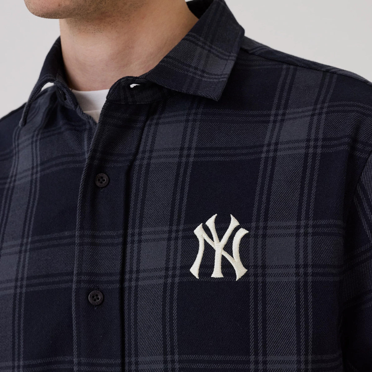 New Era New York Yankees MLB Plaid Navy Long Sleeve Shirt, front view on a model showing a navy plaid pattern with embroidered white NY logo on the chest, black button closure, and a classic collar design.
