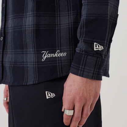 New Era New York Yankees MLB Plaid Navy Long Sleeve Shirt, close-up on a model showing the embroidered Yankees script near the hem, a New Era flag logo on the sleeve, and the dark navy plaid pattern throughout the fabric.