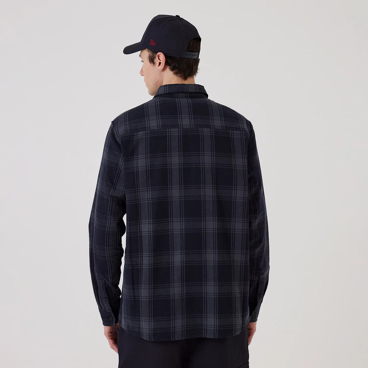 New Era New York Yankees MLB Plaid Navy Long Sleeve Shirt, back view on a model with a navy cap, showing the navy and grey checkered pattern, structured collar, and buttoned cuffs on the long sleeves, creating a classic casual look.