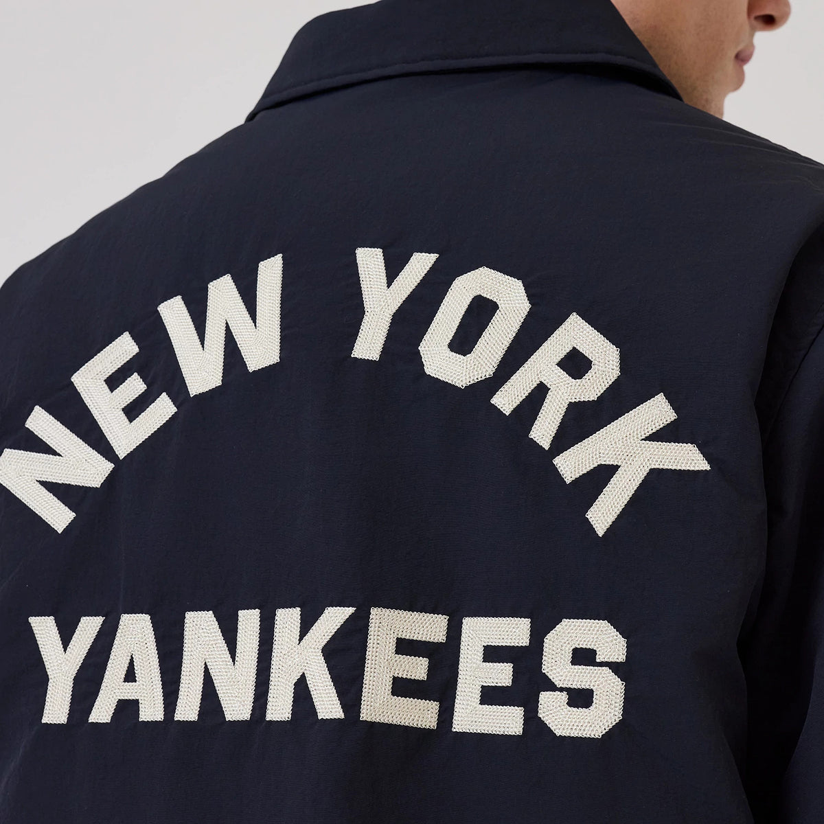 New Era New York Yankees MLB Navy Coach Jacket, back view showing large white embroidered New York Yankees lettering across the upper back, set against the deep navy fabric, with a classic collar at the top of the jacket.