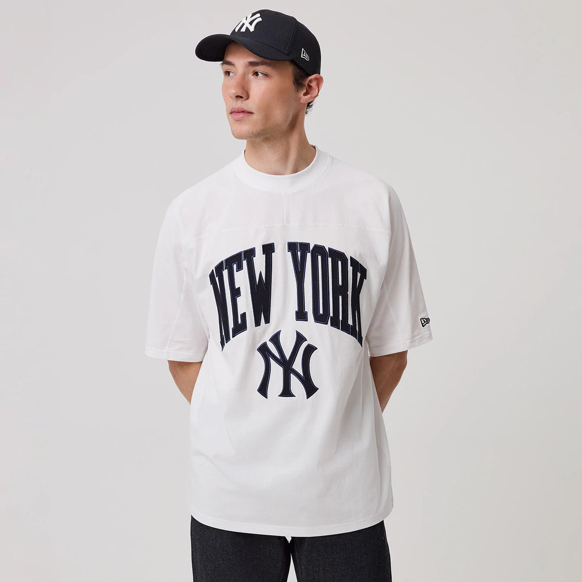 New Era New York Yankees MLB Arch Graphic White Oversized T-Shirt, front view on a model, featuring navy New York lettering arched across the chest above the interlocking NY logo, with the New Era logo embroidered on the left sleeve.