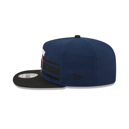 New York Knicks NBA Tip Off 2026 Dark Blue New Era 9FIFTY A-Frame Snapback Adjustable Cap, side view showing the black New Era flag logo on the left panel, structured dark blue crown with black stripes.