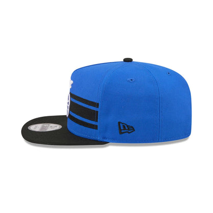 Orlando Magic NBA Tip Off 2026 Blue New Era 9FIFTY A-Frame Snapback Adjustable Cap, side view showing the embroidered black New Era flag logo on the left side, with a black flat visor and blue structured crown featuring black horizontal stripes.