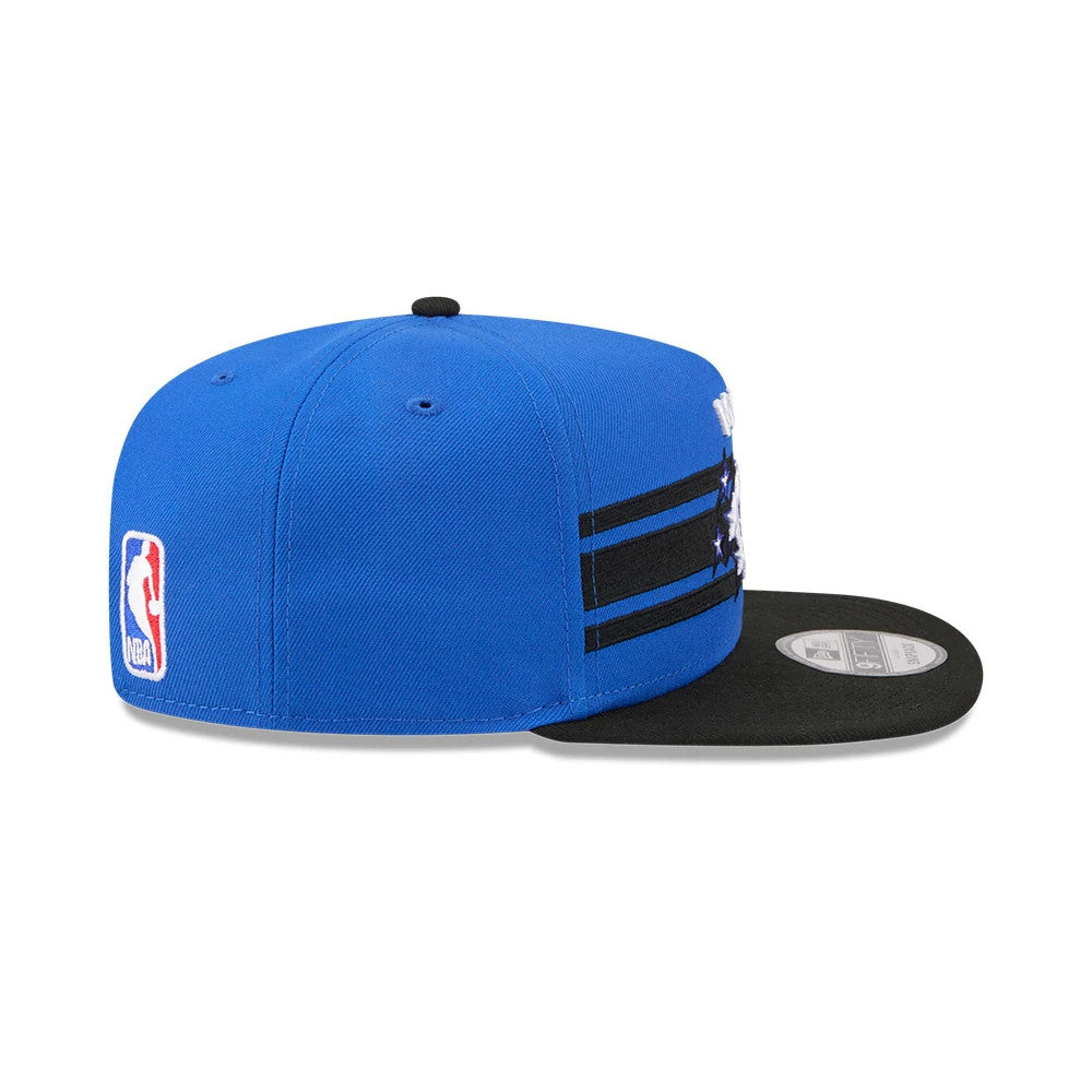 Orlando Magic NBA Tip Off 2026 Blue New Era 9FIFTY A-Frame Snapback Adjustable Cap, side view showing the NBA logo embroidered on the left side of the structured blue crown, with black stripes and a flat black visor featuring the 9FIFTY size sticker.