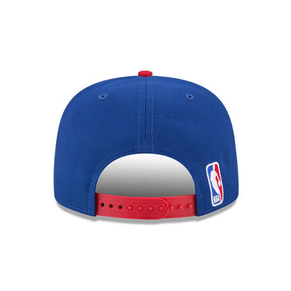 NBA Logo NBA Tip Off 2026 Blue New Era 9FIFTY A-Frame Snapback Adjustable Cap, rear view showing the white embroidered NBA logo on the lower right side, a red top button, and adjustable red snapback closure.