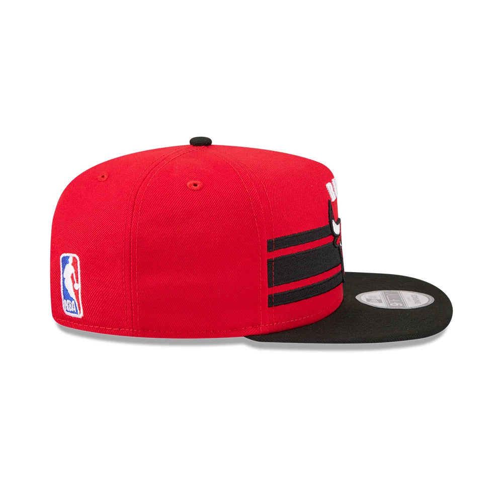 Chicago Bulls NBA Tip Off 2026 Red New Era 9FIFTY A-Frame Snapback Adjustable Cap, side view showing the embroidered NBA logo on the left side, the structured red crown with black stripes, and the flat black visor with a 9FIFTY size sticker.