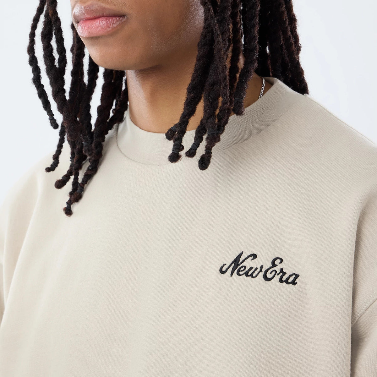 New Era Open Hem Light Beige Oversized Crew Neck Sweater, front view on a model with the classic New Era script logo embroidered in black on the left chest, featuring a relaxed fit and ribbed collar.
