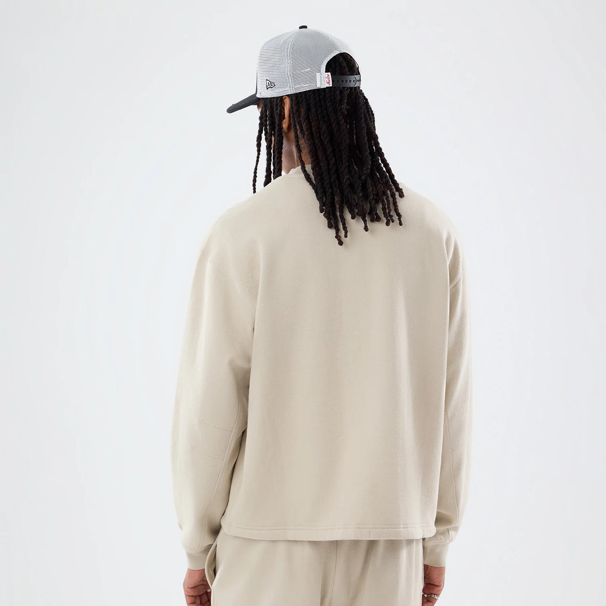 New Era Open Hem Light Beige Oversized Crew Neck Sweater, rear view on a model with a grey cap, showing the relaxed fit of the sweater, its light beige colour, and the open hem design.
