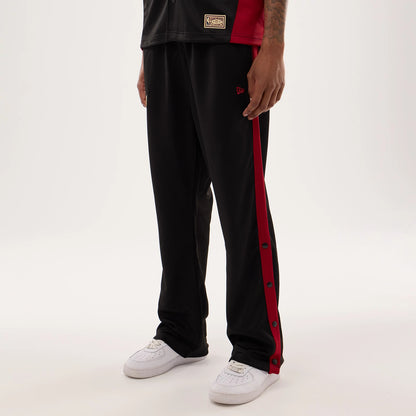 New Era Miami Heat NBA Hardwood Classic Straight Black Straight Leg Joggers, on-model view with black fabric and red side stripe featuring buttons, embroidered red New Era flag logo on the upper leg, paired with white trainers.