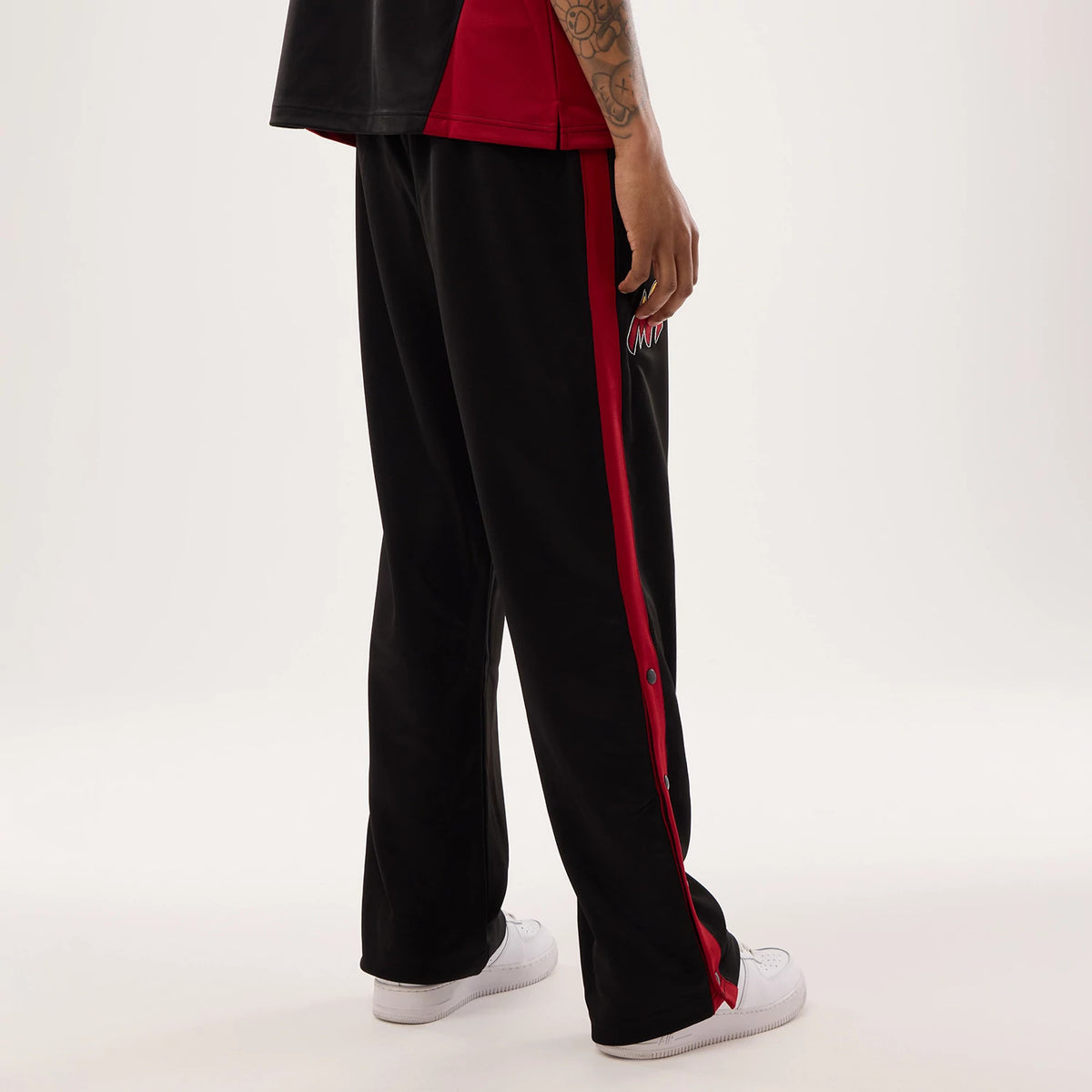 New Era Miami Heat NBA Hardwood Classic Straight Black Straight Leg Joggers, side view on a model showing the black joggers with a red side stripe and buttons, featuring the Miami Heat logo embroidered near the side seam on the upper leg.