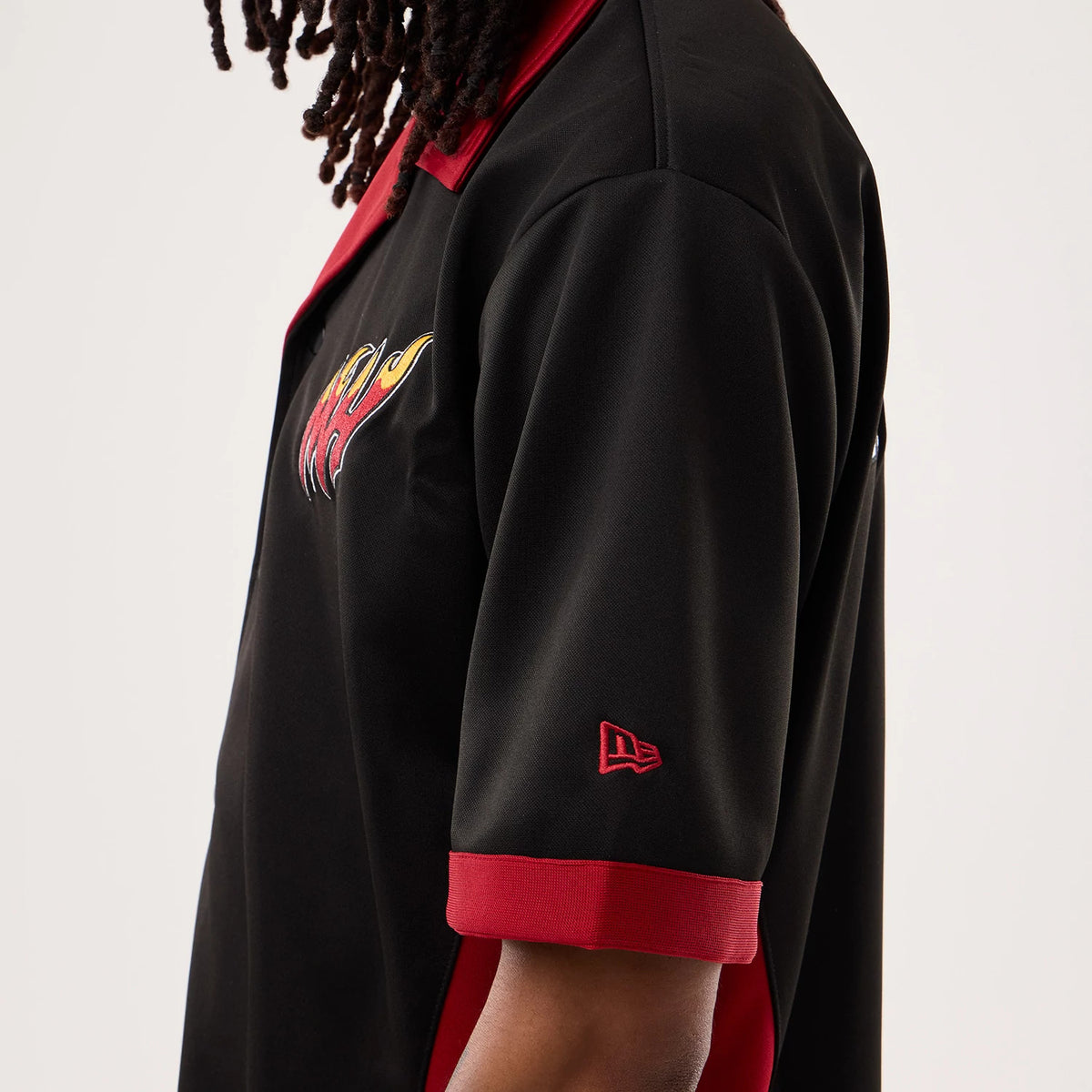 New Era Miami Heat NBA Hardwood Classic Revere Black Short Sleeve Shirt, side view on a model with a red and yellow flame logo embroidered on the chest, red New Era flag logo on the sleeve, and contrasting red collar and sleeve cuffs.