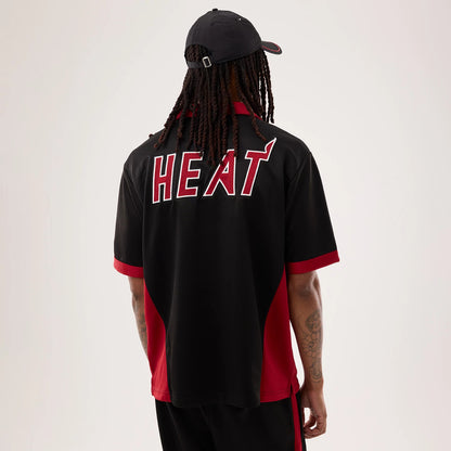 New Era Miami Heat NBA Hardwood Classic Revere Black Short Sleeve Shirt, back view on a model with a black cap, featuring large red and white HEAT lettering across the shoulders, red side panels, and matching red sleeve cuffs and collar.