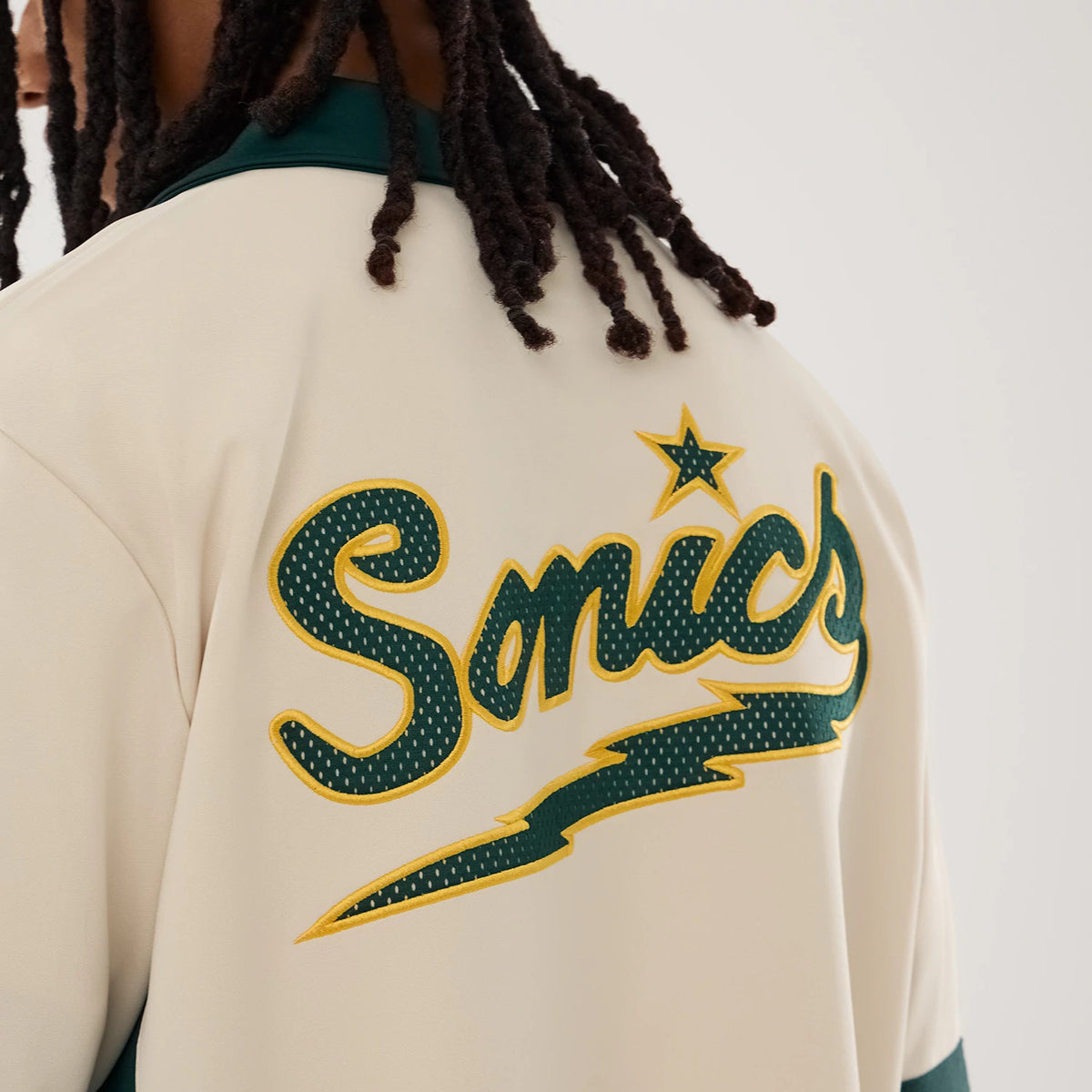 New Era Supersonics NBA Hardwood Classic Revere Beige Short Sleeve Shirt, back view on a model featuring a large green and yellow embroidered Sonics script with a star above it on the upper back, complemented by a dark green collar.