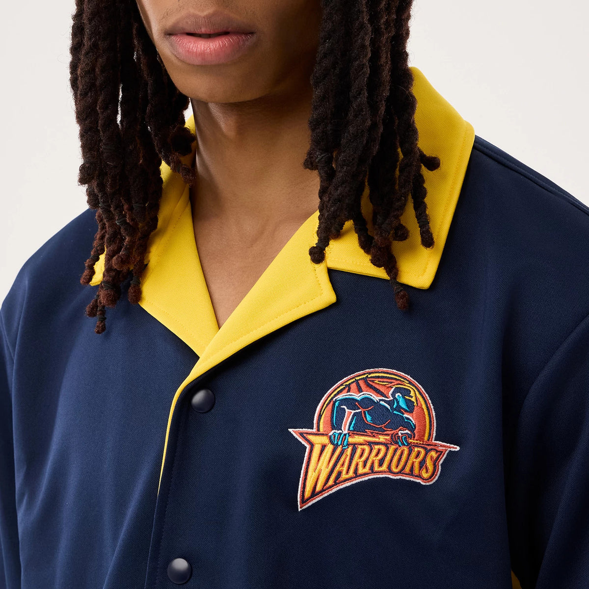 New Era Warriors NBA Hardwood Classic Revere Dark Blue Short Sleeve Shirt, front view on a model displaying the embroidered Warriors logo on the left chest, featuring a dark blue fabric with eye-catching contrast yellow collar.