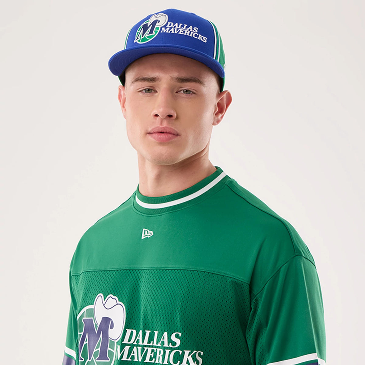New Era Dallas Mavericks NBA Hardwood Classic Mesh Oversized Green T-Shirt, front view on a model wearing a blue cap, featuring the large printed Mavericks logo on the chest, a small embroidered New Era logo on the upper chest.